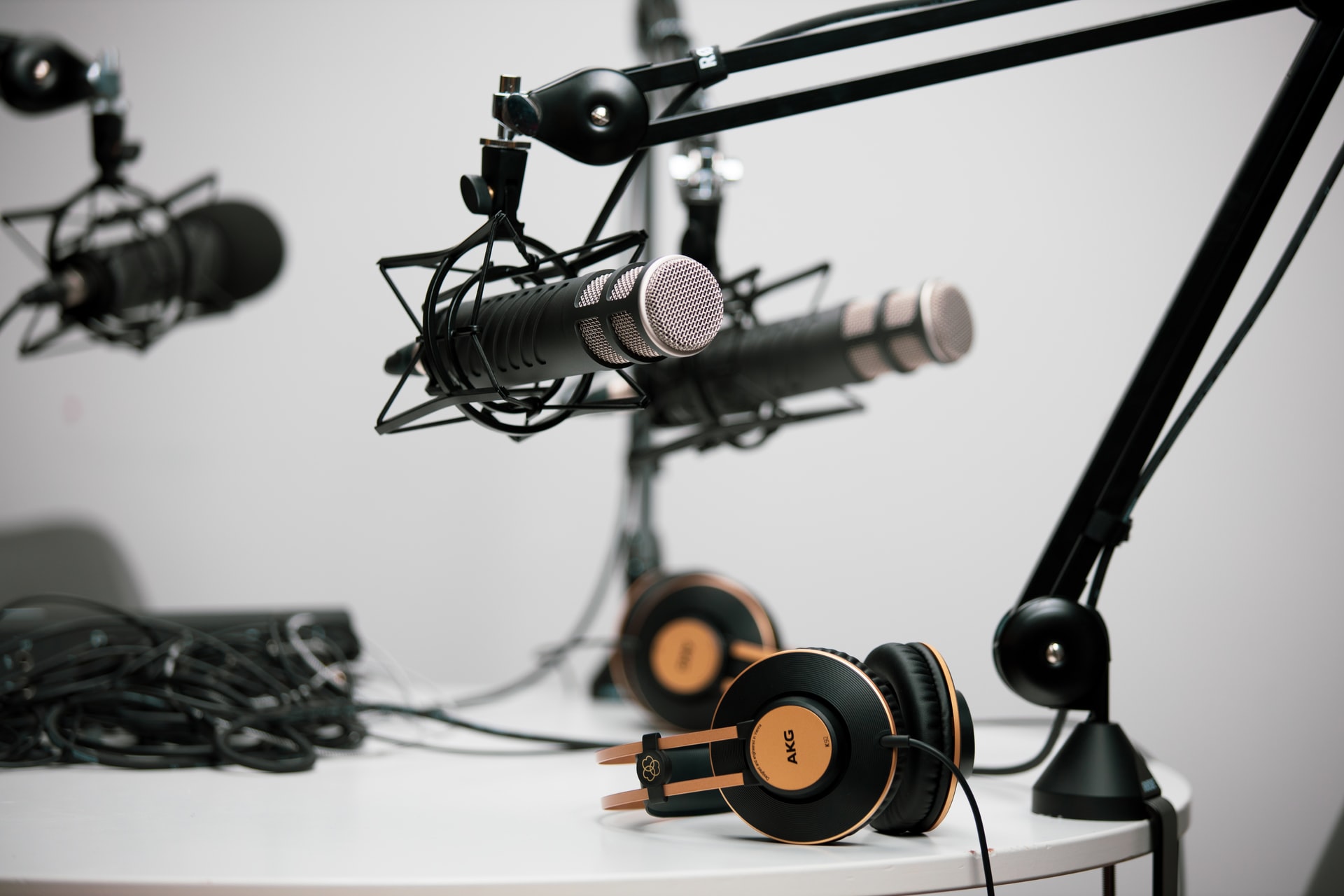 Three podcasting microphones on boom arms at a teble with headphones in shot. 