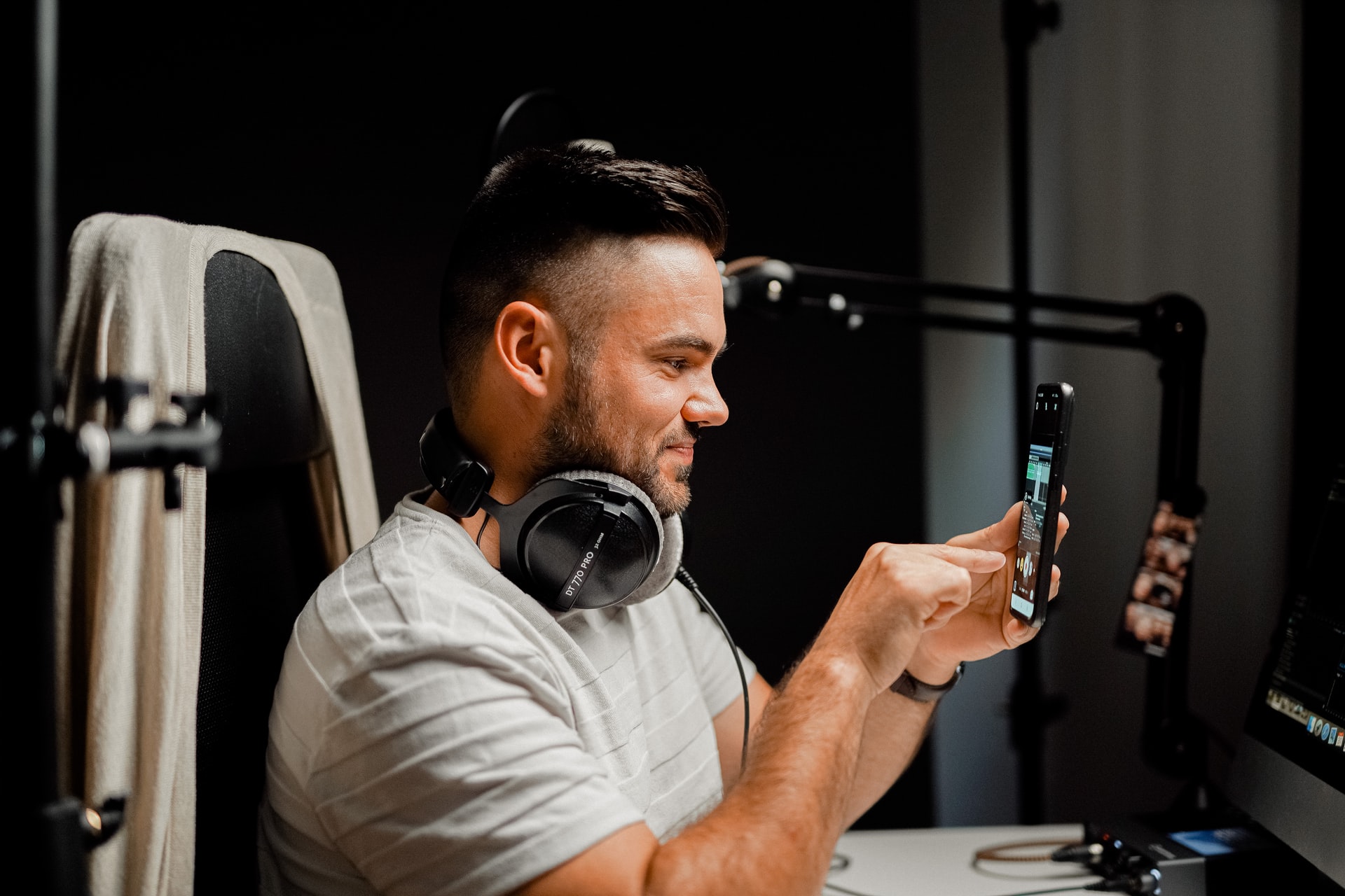 man recording an instagram story with headphones in front of a smartphone with podcast gear like headphones, an interface and a microphone stand