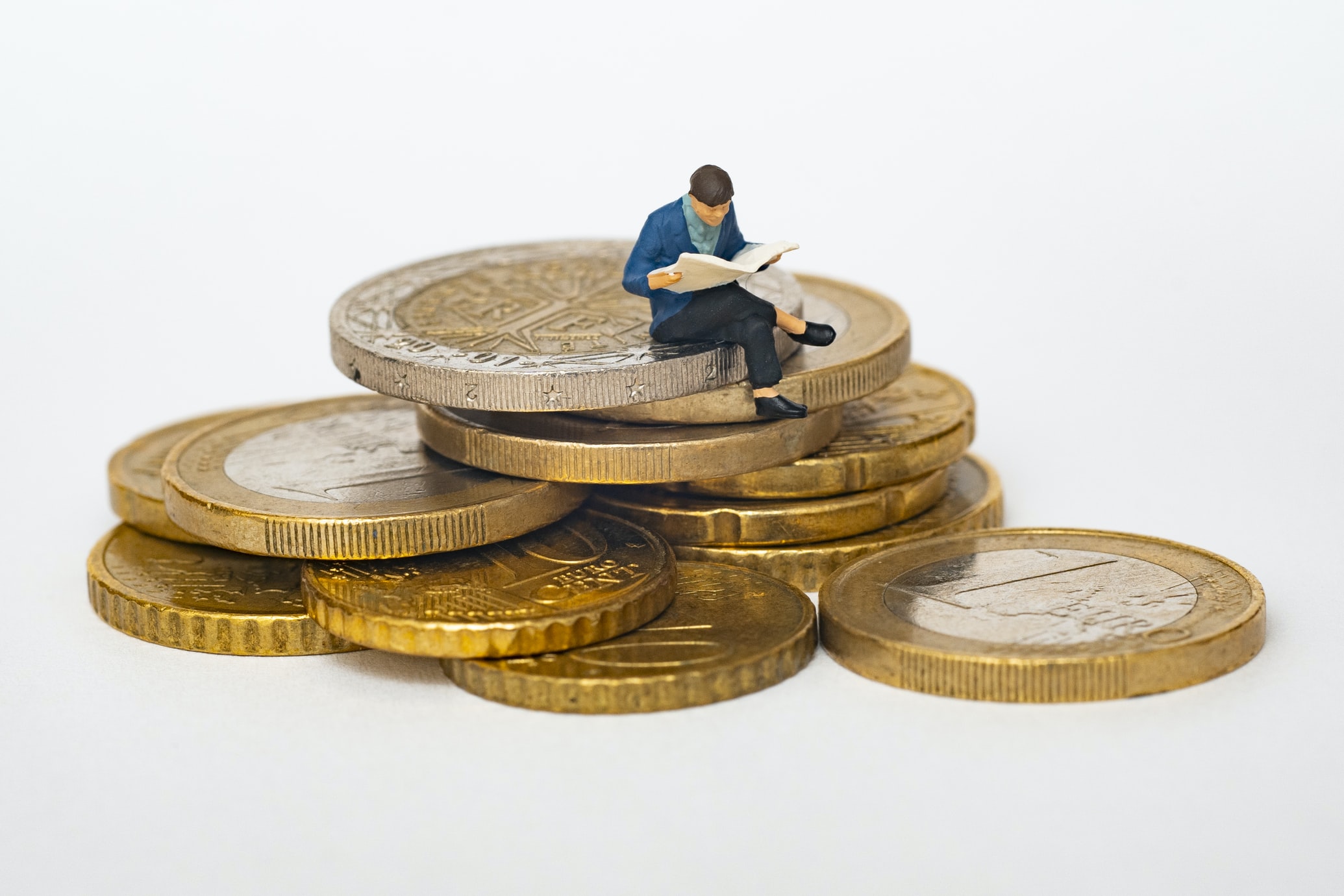  a miniature figurine reading a newspaper on top of a stack of coins