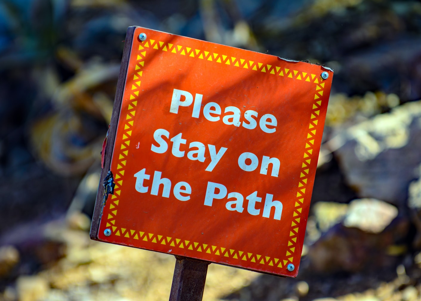 a red sign directing people to stay on the path