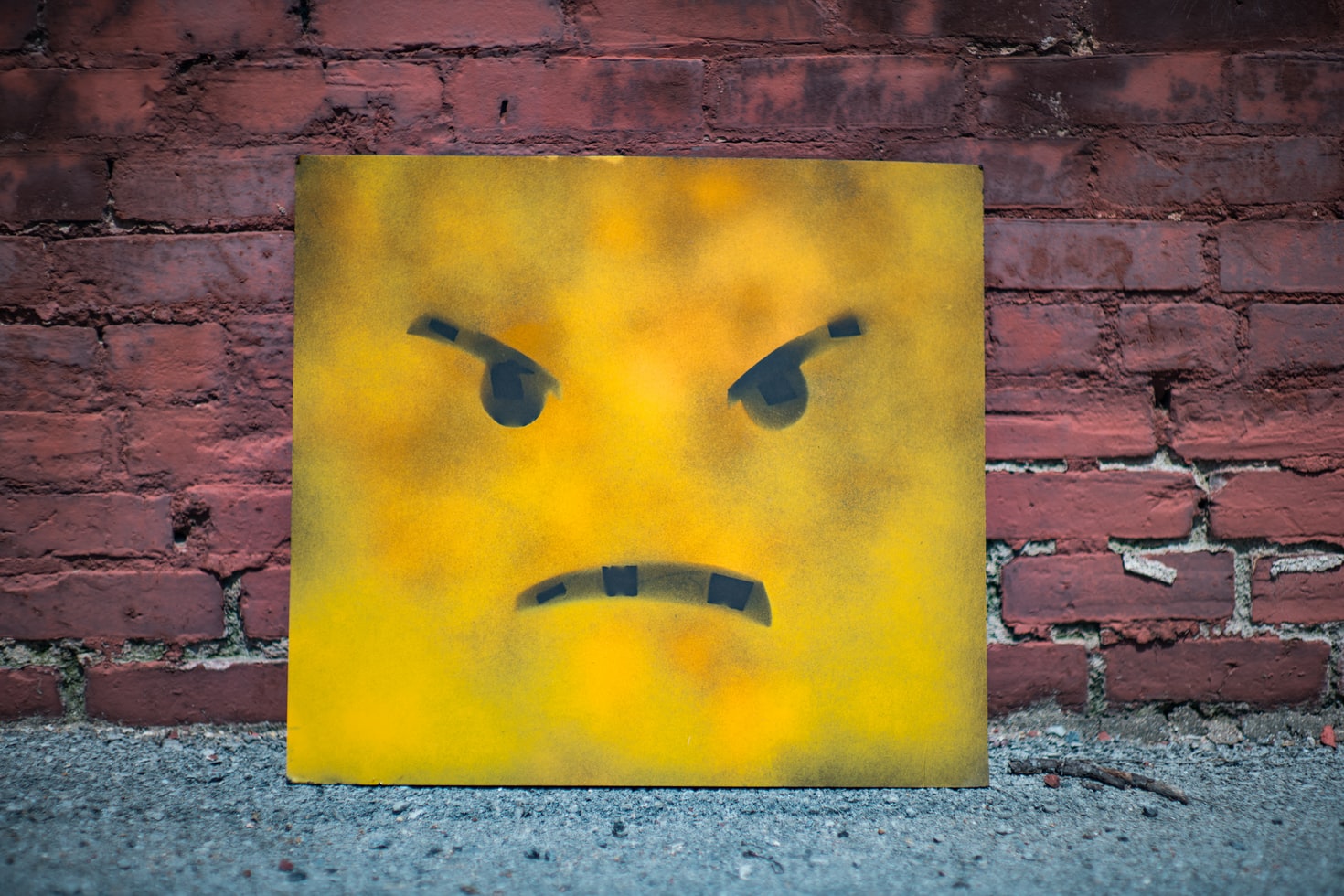 yellow and black smiley painting leaned against a brick wall