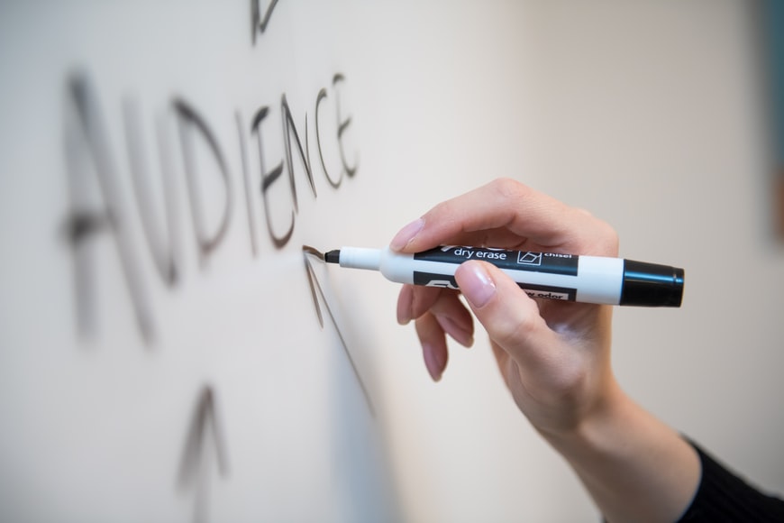 a person writing the word “audience” on a whiteboard
