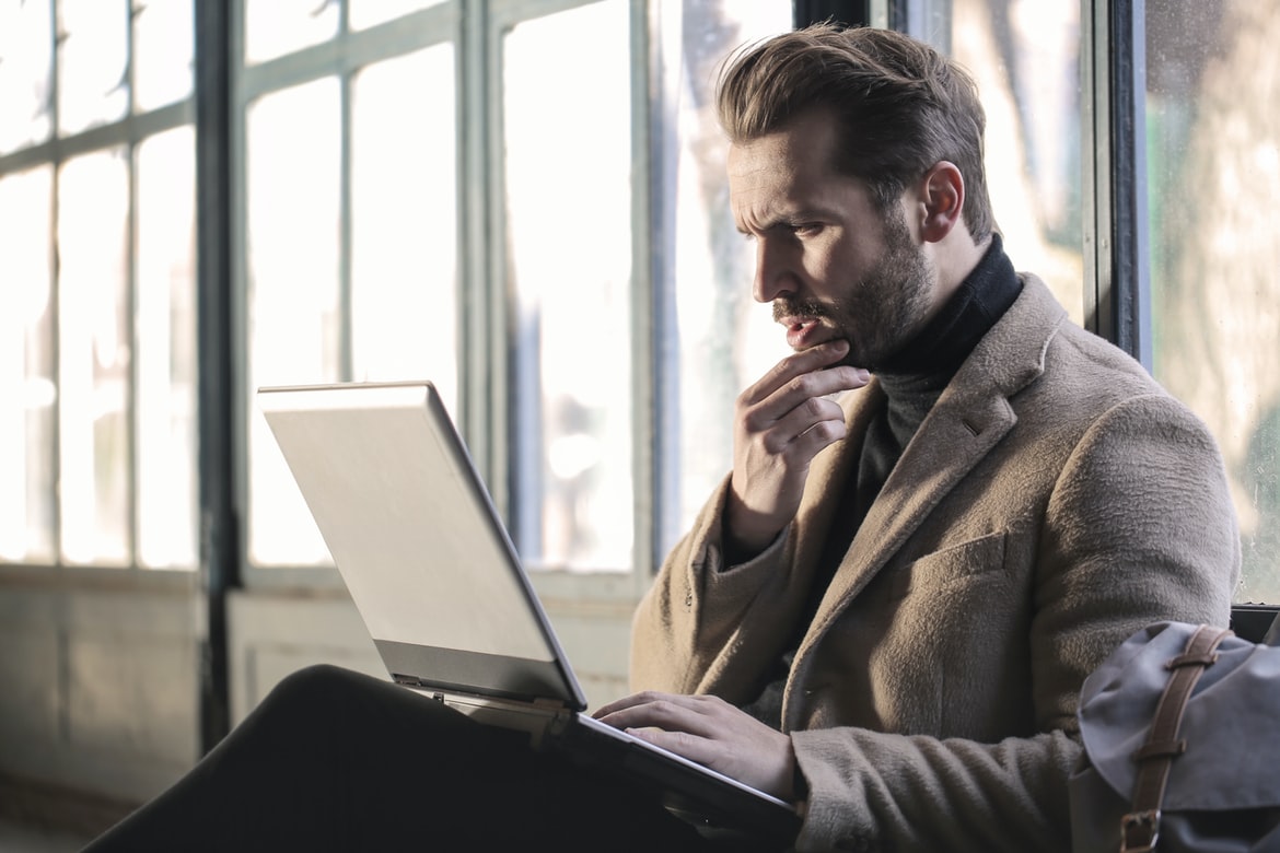 man squinting at a laptop and thinking