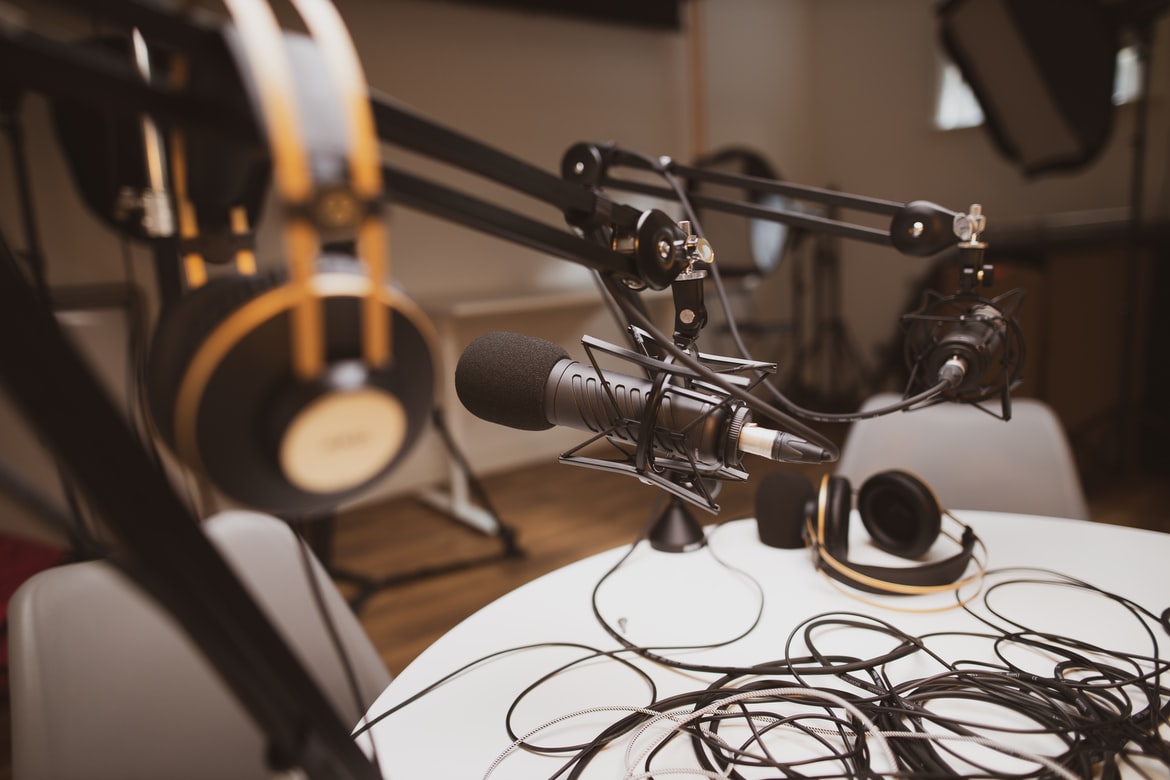 Podcasting setup with headphones, wires, and professional microphones around a table.